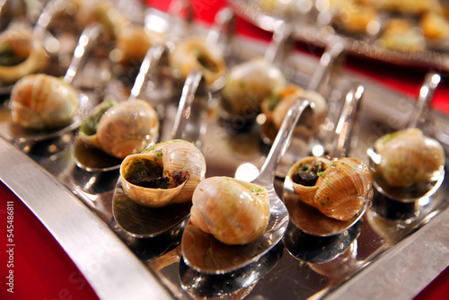 Escargots de Bourgogne.  Baked snails with garlic. French traditional food. Catering banquet. Table with escargots on spoons at a banquet