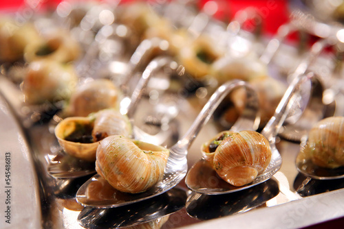 Escargots de Bourgogne.  Baked snails with garlic. French traditional food. Catering banquet. Table with escargots on spoons at a banquet