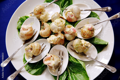 Escargots de Bourgogne. Stuffed snails with butter and garlic. Hot gourmet dish in French traditional with spoons and forks on white platter. Banquet event