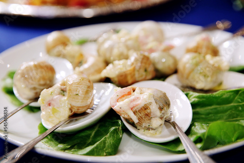 Escargots de Bourgogne. Stuffed snails with butter and garlic. Hot gourmet dish in French traditional with spoons and forks on white platter. Banquet event