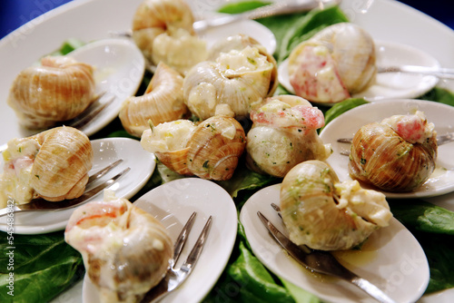 Escargots de Bourgogne. Stuffed snails with butter and garlic. Hot gourmet dish in French traditional with spoons and forks on white platter. Banquet event