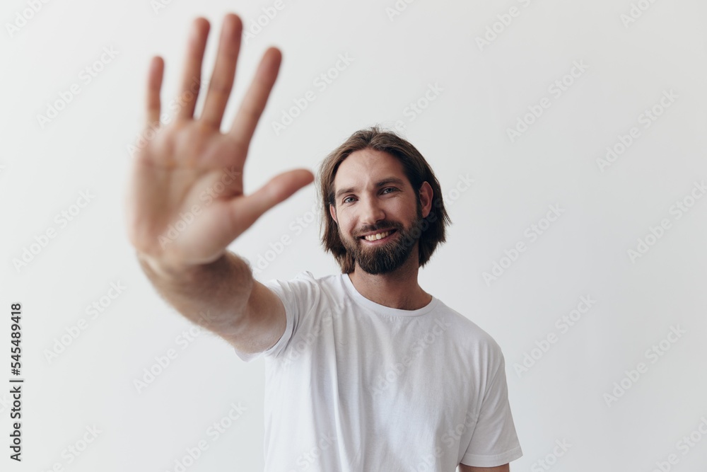 Happy adult man with a beard smiles and pulls the cook into the camera listening to music in headphones in a distressed t-shirt on a white isolated background Happy adult man with a beard smiles and pulls the cook into the camera listening to music in headphones in a distressed t-shirt on a white isolated background
