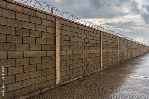 Photography Brick wall that is lost from sight along, equipped in its upper part with concertinas, wires with cutting blades as an obstacle to cross it