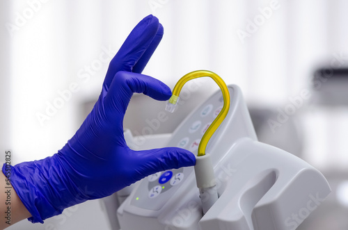Saliva ejector and a hand in a disposable glove symbolize love in dentistry. Hand in a blue glove. Yellow saliva ejector. With love in dentistry. Heart symbol. Symbol of Ukraine.