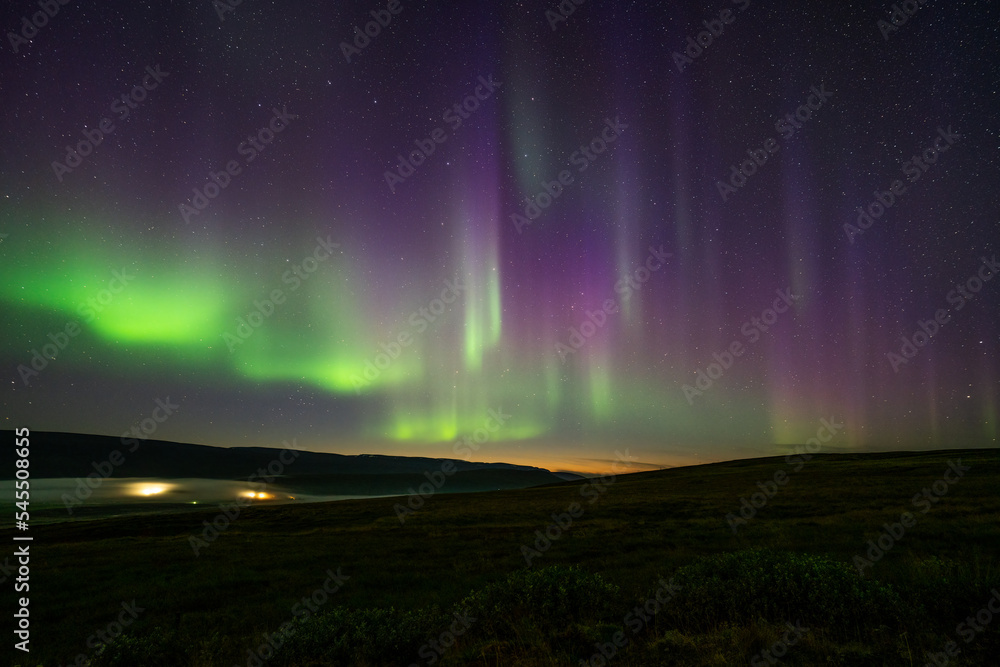 colorful northern light (Aurora) in the night sky with mountain, fog, horizon and small village