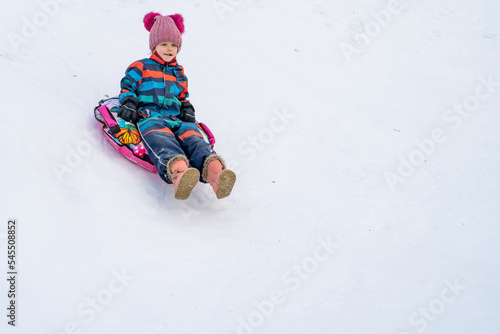 Little girl sliding downhill on tube. Child sledding in winter hill.