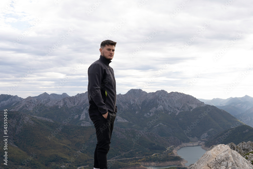 The young mountaineer dressed in dark mountain clothing at the top of the mountain. The background scenery is breathtaking and steep mountains are visible. Wallpapers for hiking and climbing.