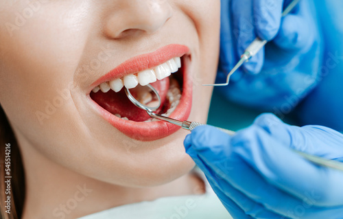 Attractive young woman with natural white teeth in dental clinic. Hands doctor dentist with medical tools. Healthy teeth concept