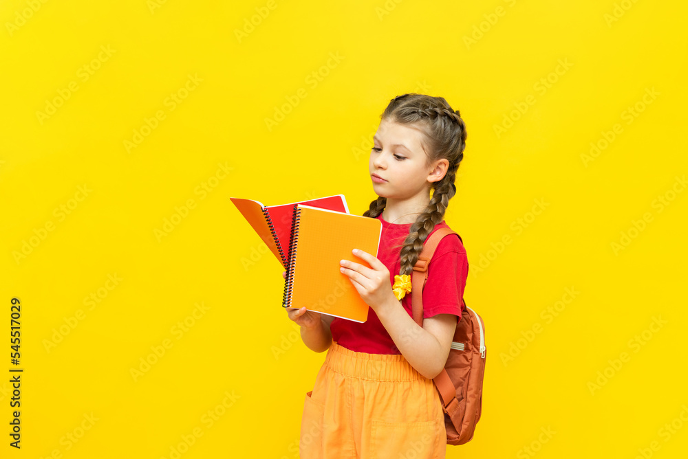A schoolgirl with a backpack and notebooks is preparing for additional training courses. A beautiful little girl is going to school on a yellow isolated background. A schoolgirl with a backpack and notebooks is preparing for additional training courses. A beautiful little girl is going to school on a yellow isolated background.
