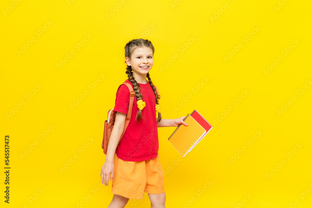 A schoolgirl with a backpack and textbooks. Preparing a student for exams. A little girl is going to school on a yellow isolated background. Children's education. A schoolgirl with a backpack and textbooks. Preparing a student for exams. A little girl is going to school on a yellow isolated background. Children's education.