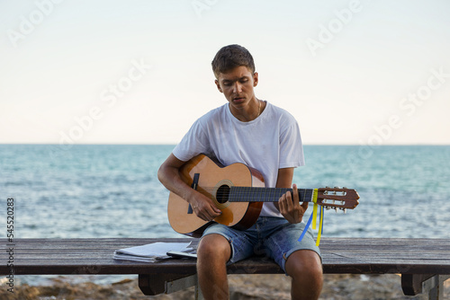 A young stylish guy plays the guitar on the embankment by the sea, the concept of music and relaxation