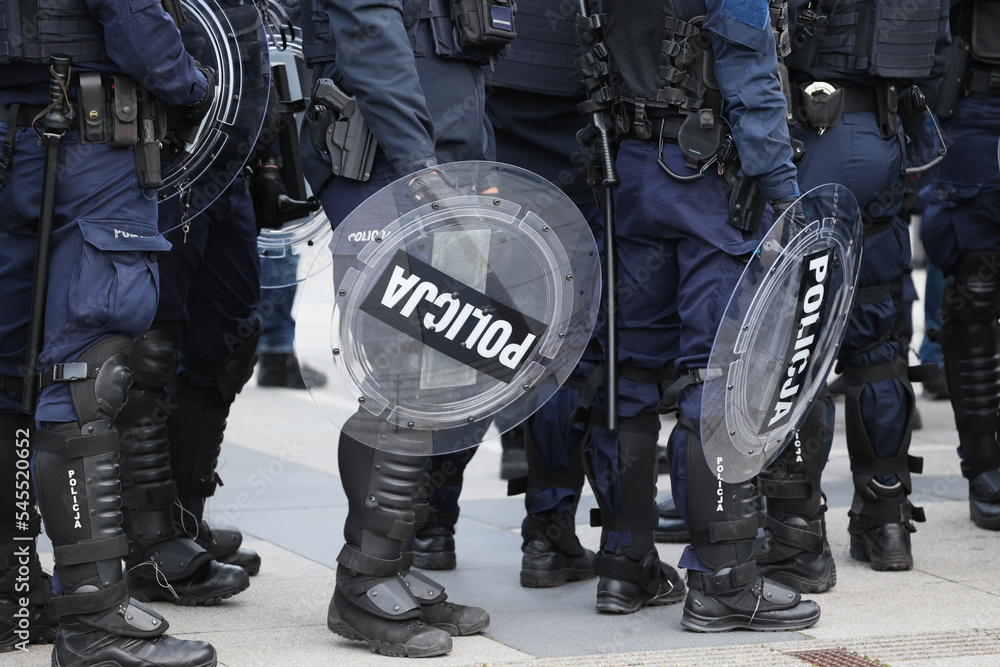 Policjanci prewencji w mundurach i tarczami idą na akcję w szeregu.  - obrazy, fototapety, plakaty 