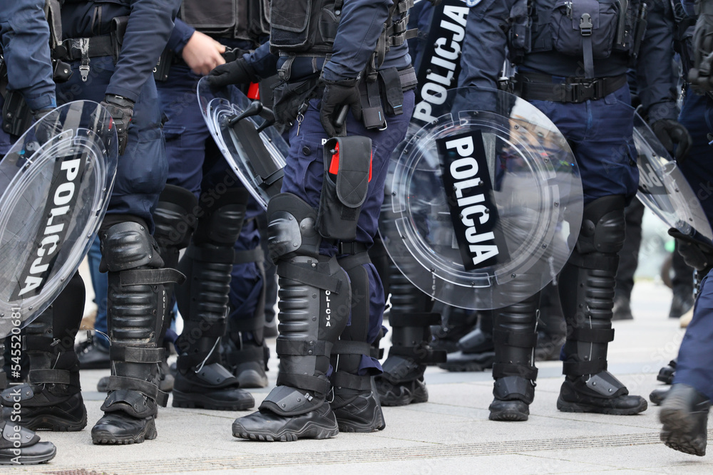 Policjanci prewencji w mundurach i tarczami idą na akcję w szeregu.  - obrazy, fototapety, plakaty 