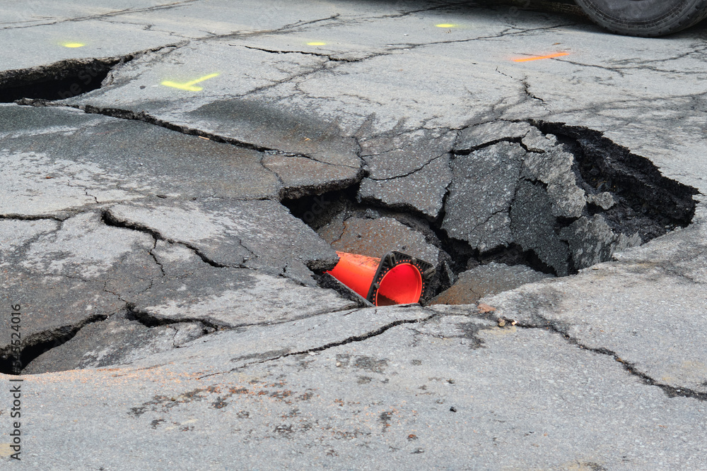 Sink hole in middle of asphalt street following collapse of road Sink hole in middle of asphalt street following collapse of road