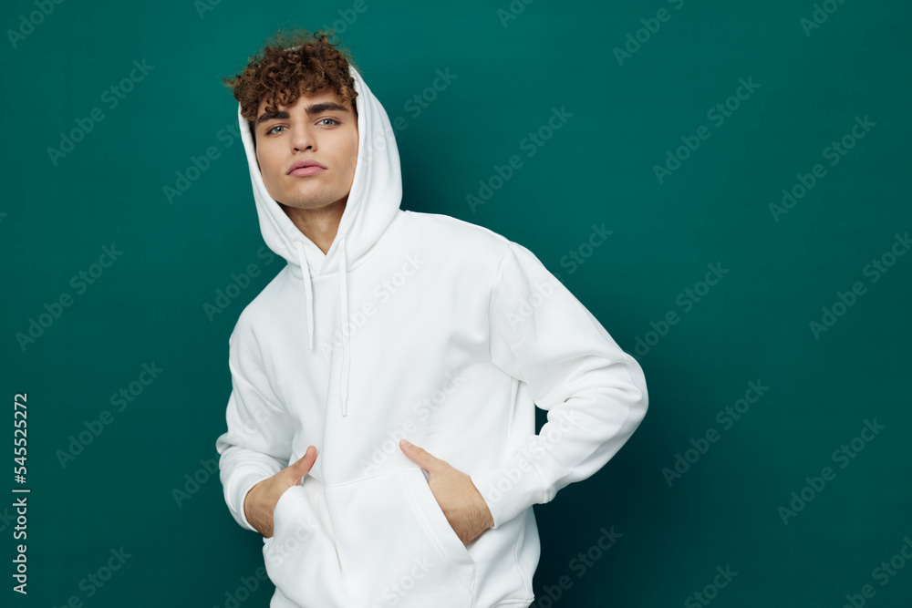 a handsome man stands on a green background in a white hoodie with a hood on his head and keeps his hands in the pocket of the hoodie a handsome man stands on a green background in a white hoodie with a hood on his head and keeps his hands in the pocket of the hoodie