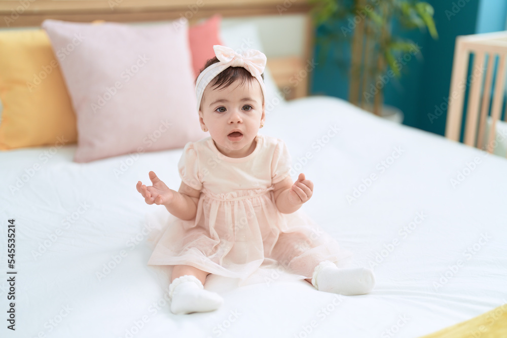 Adorable toddler sitting on bed with relaxed expression at bedroom Adorable toddler sitting on bed with relaxed expression at bedroom