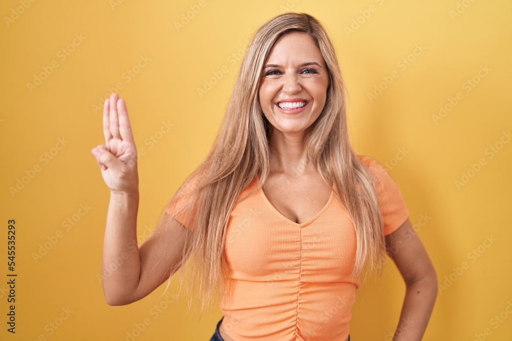 Young woman standing over yellow background showing and pointing up with fingers number three while smiling confident and happy. Young woman standing over yellow background showing and pointing up with fingers number three while smiling confident and happy.