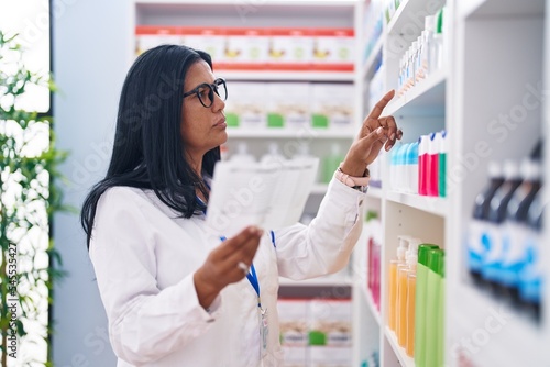 Middle age hispanic woman pharmacist reading prescription at pharmacy