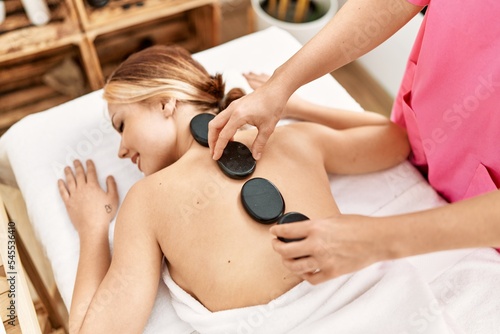 Young caucasian woman lying on table having back massage using hot stones at beauty salon
