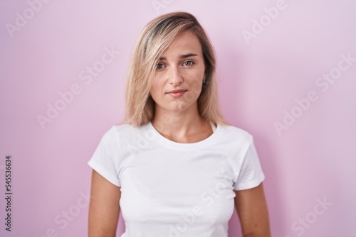 Young blonde woman standing over pink background with hands together and crossed fingers smiling relaxed and cheerful. success and optimistic © Krakenimages.com