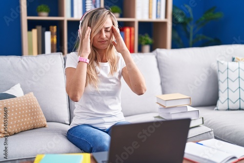 Young blonde woman studying using computer laptop at home with hand on head, headache because stress. suffering migraine.