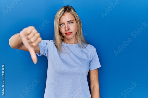 Beautiful blonde woman wearing casual t shirt over blue background looking unhappy and angry showing rejection and negative with thumbs down gesture. bad expression. © Krakenimages.com