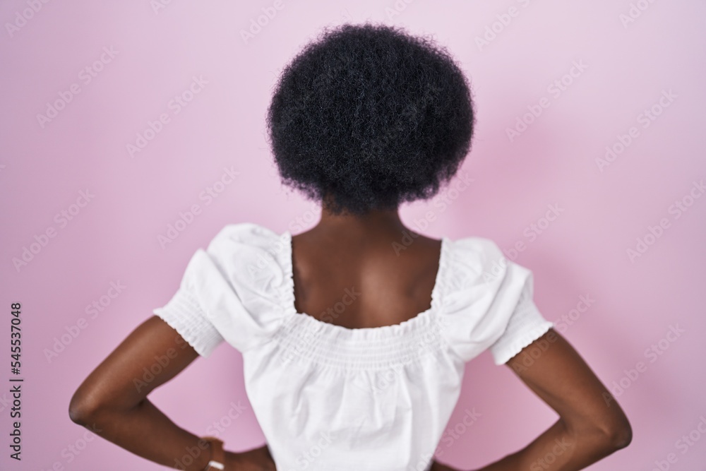 African woman with curly hair standing over pink background standing backwards looking away with arms on body African woman with curly hair standing over pink background standing backwards looking away with arms on body