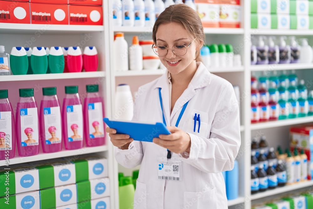 Young blonde woman pharmacist using touchpad working at pharmacy