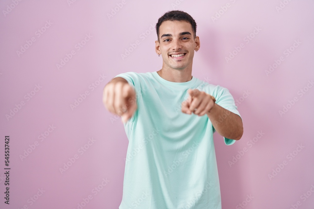 Handsome hispanic man standing over pink background pointing to you and the camera with fingers, smiling positive and cheerful Handsome hispanic man standing over pink background pointing to you and the camera with fingers, smiling positive and cheerful