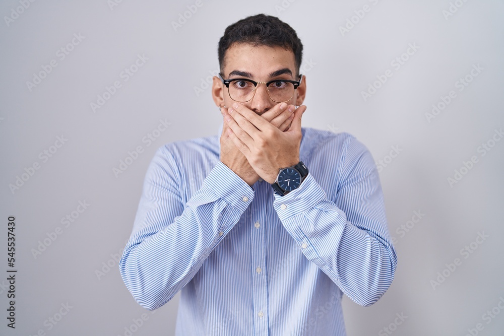 Handsome hispanic man wearing business clothes and glasses shocked covering mouth with hands for mistake. secret concept. Handsome hispanic man wearing business clothes and glasses shocked covering mouth with hands for mistake. secret concept.