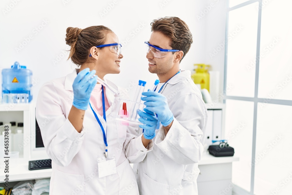 Man and woman wearing scientist uniform holding test tube at laboratory Man and woman wearing scientist uniform holding test tube at laboratory