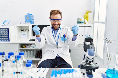 Middle age man working at scientist laboratory very happy and excited doing winner gesture with arms raised, smiling and screaming for success. celebration concept.