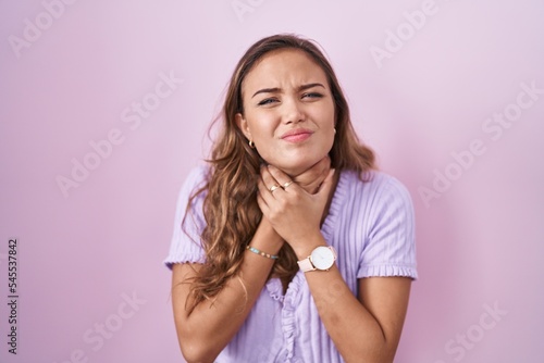 Young hispanic woman standing over pink background shouting suffocate because painful strangle. health problem. asphyxiate and suicide concept.