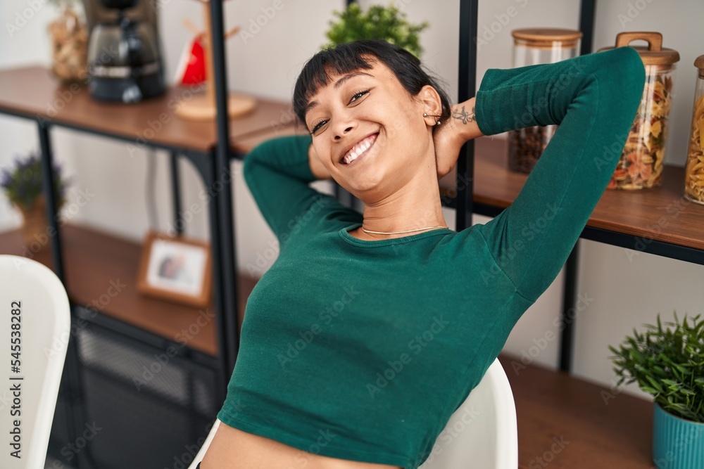 Fototapeta premium Young beautiful hispanic woman relaxed with hands on head sitting on table at home