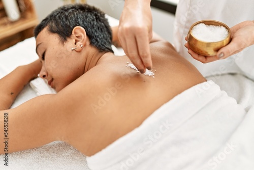 Young hispanic woman having back massage using salt at beauty center