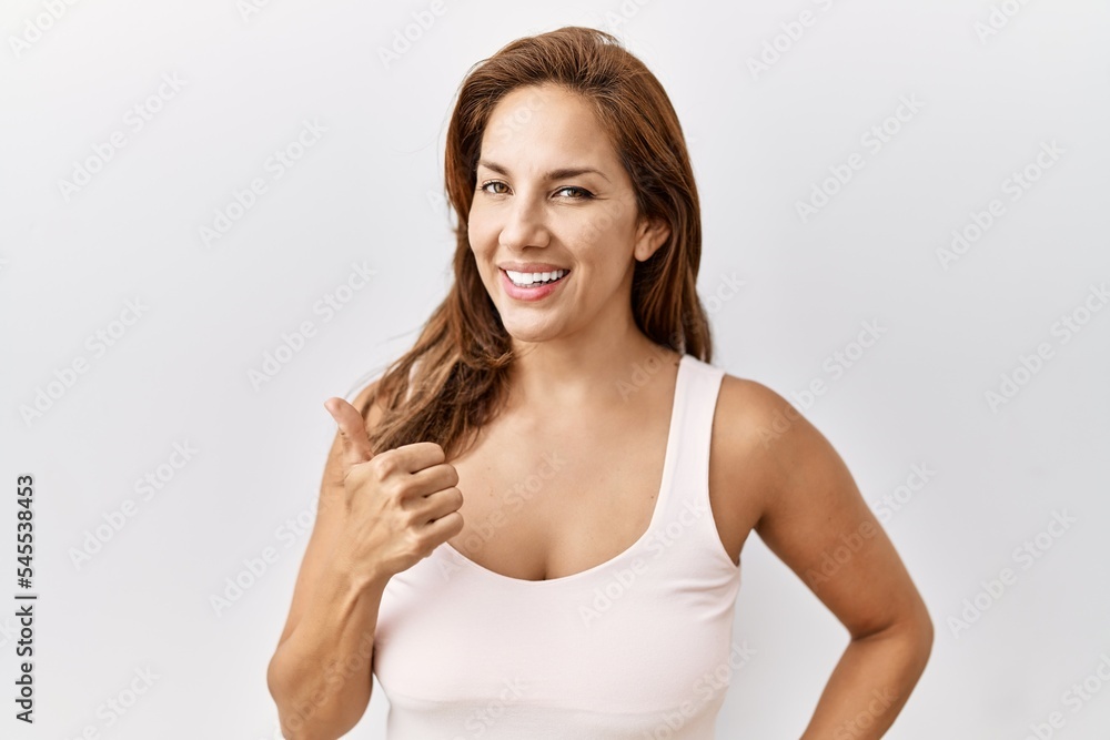 Middle age hispanic woman standing over isolated background doing happy thumbs up gesture with hand. approving expression looking at the camera showing success. Middle age hispanic woman standing over isolated background doing happy thumbs up gesture with hand. approving expression looking at the camera showing success.