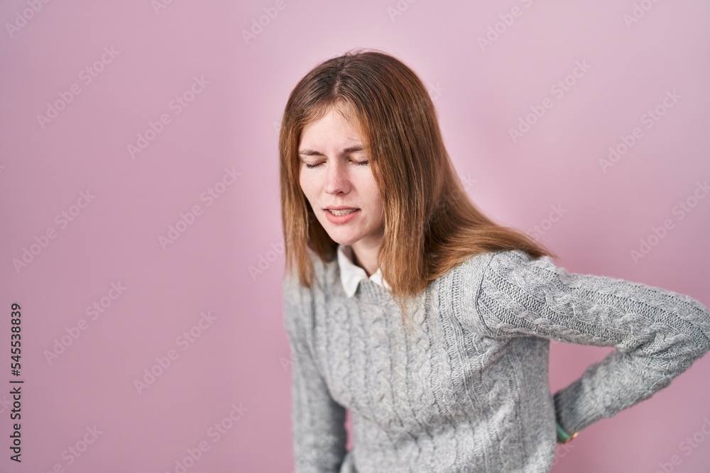 Beautiful woman standing over pink background suffering of backache, touching back with hand, muscular pain Beautiful woman standing over pink background suffering of backache, touching back with hand, muscular pain