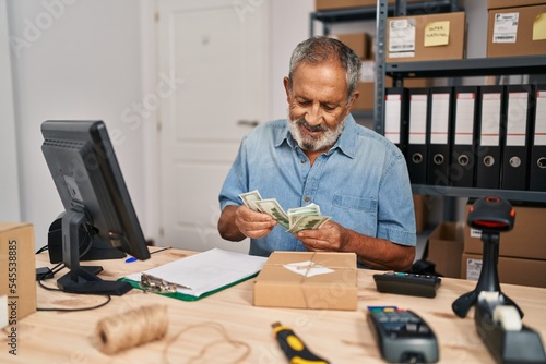Senior grey-haired man ecommerce business worker counting dollars at office