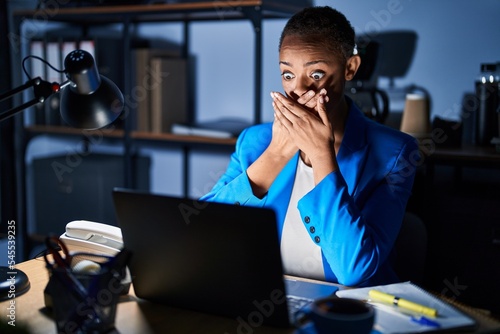 Beautiful african american woman working at the office at night shocked covering mouth with hands for mistake. secret concept.