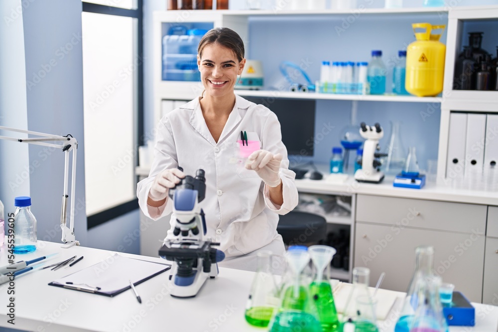 Young beautiful hispanic woman scientist using microscope holding sample at laboratory Young beautiful hispanic woman scientist using microscope holding sample at laboratory