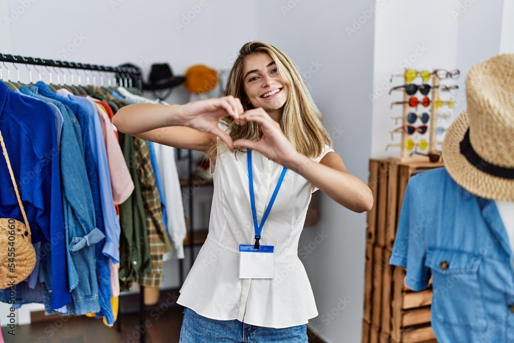 Young blonde woman working as manager at retail boutique smiling in love doing heart symbol shape with hands. romantic concept. Young blonde woman working as manager at retail boutique smiling in love doing heart symbol shape with hands. romantic concept.