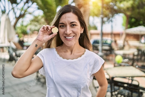 Young hispanic woman smiling confident holding bitcoin at park