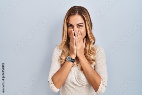 Young blonde woman standing over isolated background laughing and embarrassed giggle covering mouth with hands, gossip and scandal concept