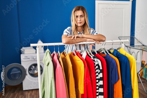 Young blonde woman at laundry room with clean clothes skeptic and nervous, frowning upset because of problem. negative person.