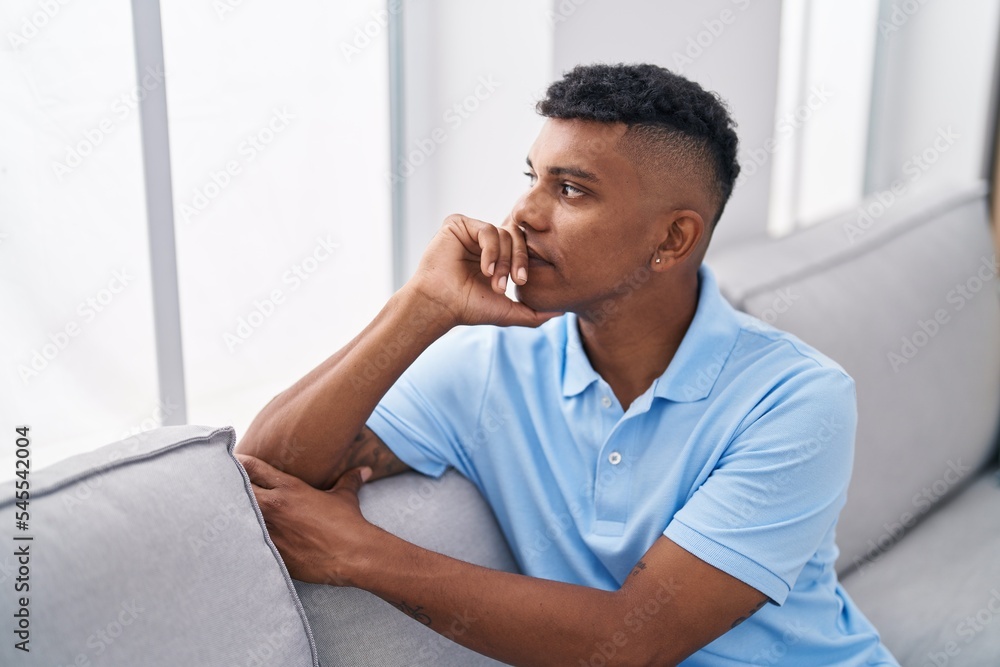 Young latin man looking to the window sitting on sofa at home