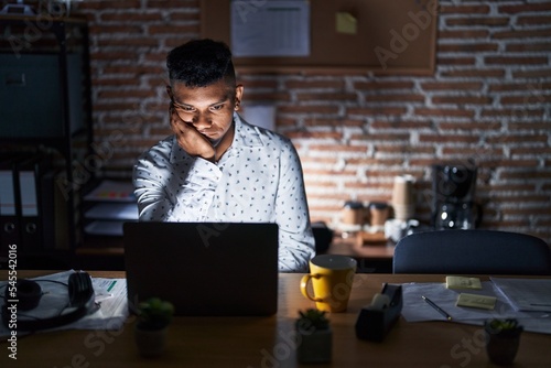 Young hispanic man working at the office at night thinking looking tired and bored with depression problems with crossed arms.