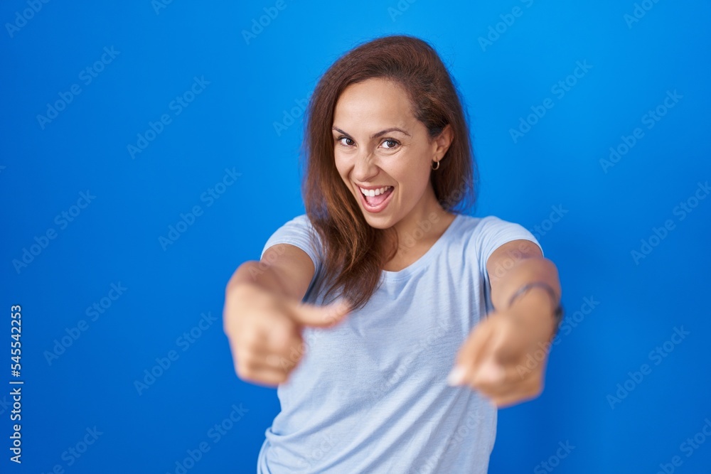 Fototapeta premium Brunette woman standing over blue background pointing fingers to camera with happy and funny face. good energy and vibes.