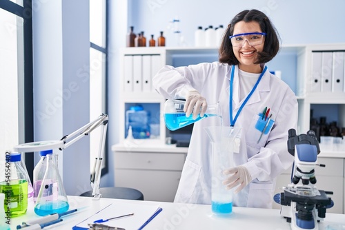 Young woman scientist pouring liquid on test tube at laboratory