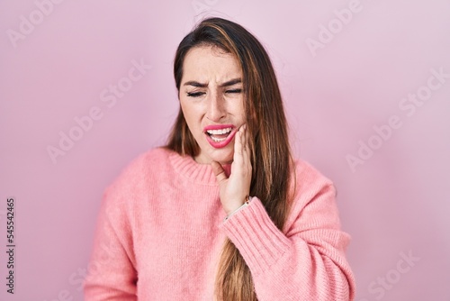 Young hispanic woman standing over pink background touching mouth with hand with painful expression because of toothache or dental illness on teeth. dentist © Krakenimages.com