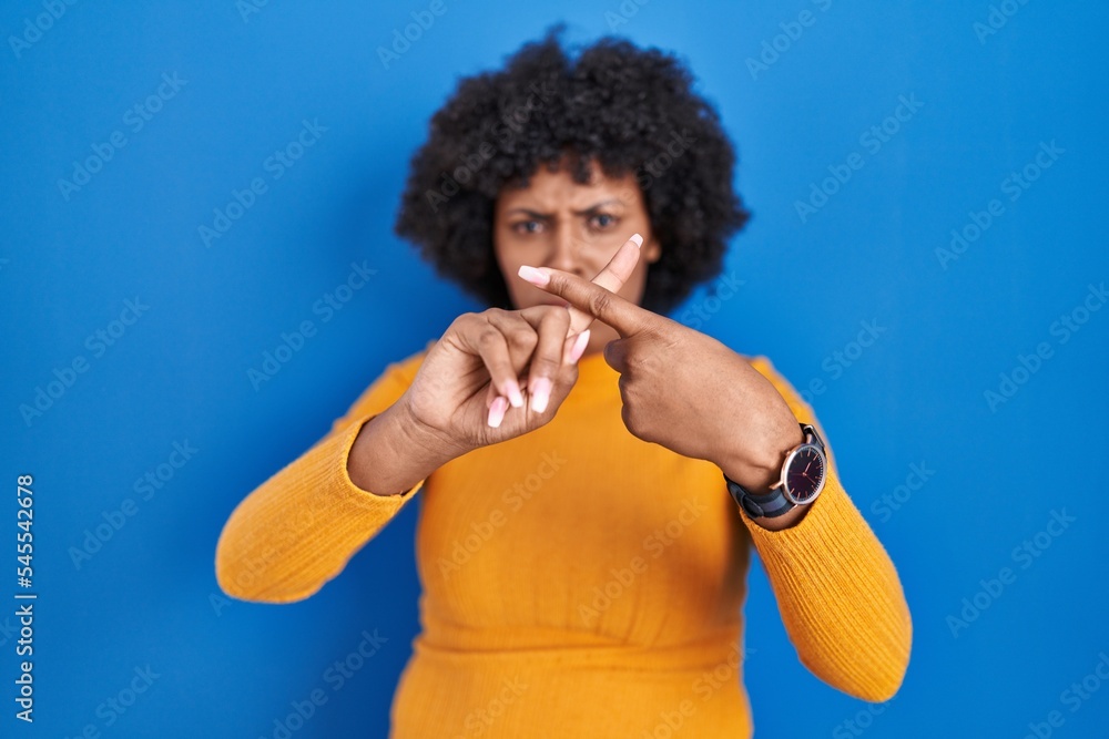 Black woman with curly hair standing over blue background rejection expression crossing fingers doing negative sign Black woman with curly hair standing over blue background rejection expression crossing fingers doing negative sign